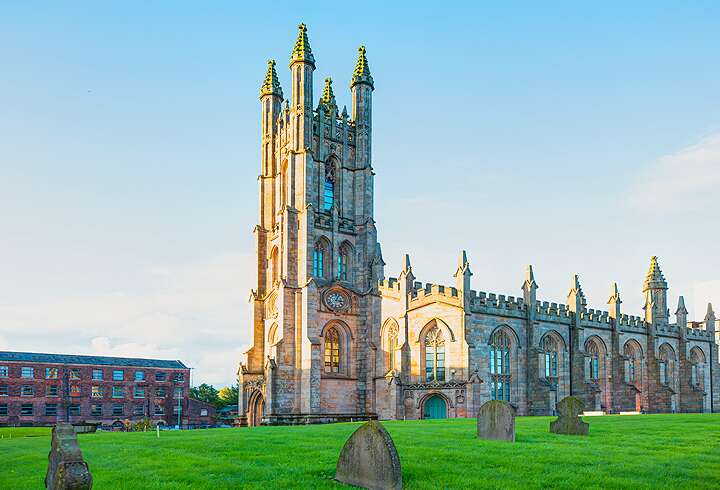 Manchesterin katedraali kuvattuna kesäpäivänä vehreän nurmialueen ympäröimänä..