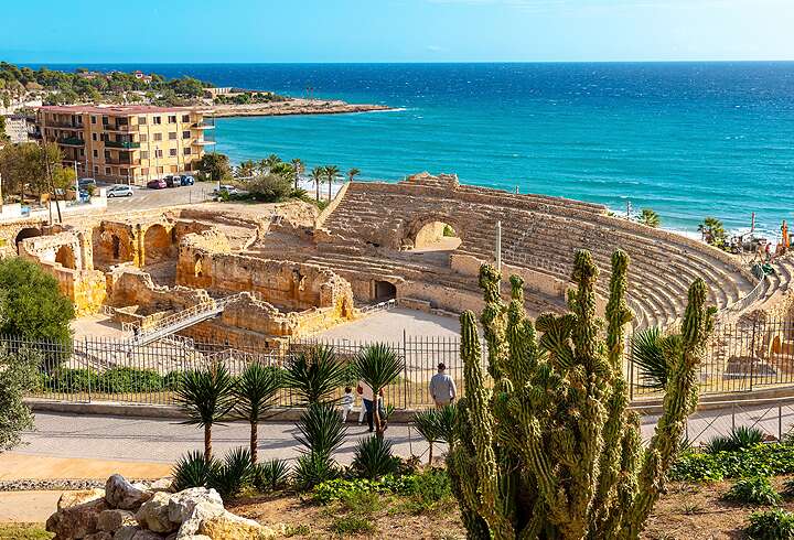Roomalainen amfiteatteri Tarragonassa Espanjan Kataloniassa auringonpaisteessa ja taustalla siintää turkoosi Välimeri.