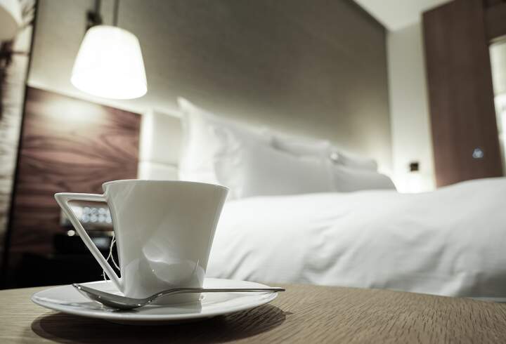 Tyylikäs hotellihuone jossa sängyn vieressä kahvikuppi.